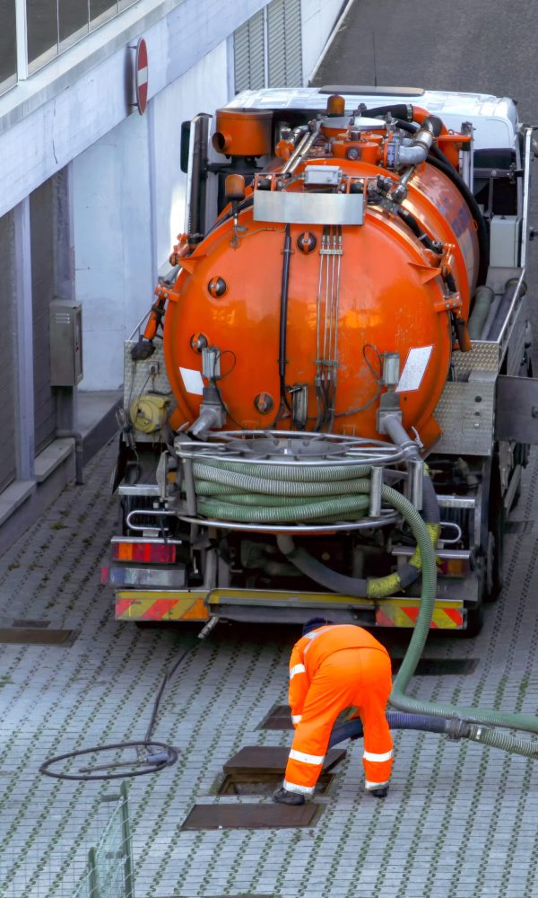 Worker lowers sewer hose into sewer pit.